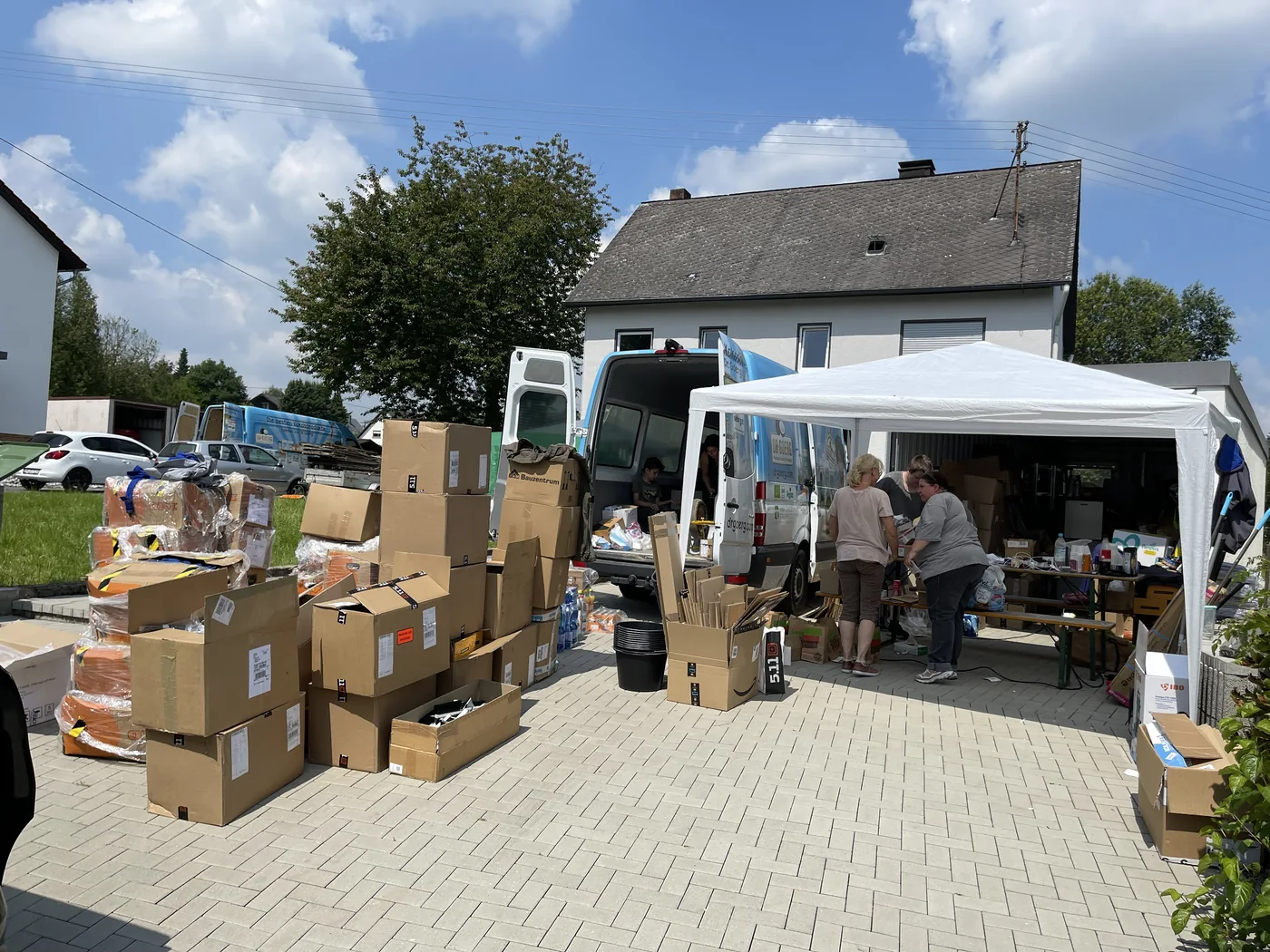 Spendenumschlag im Juli 2021: Helfer sortieren Kartons und Hilfsgüter zwischen Transportern und einem Pavillon
